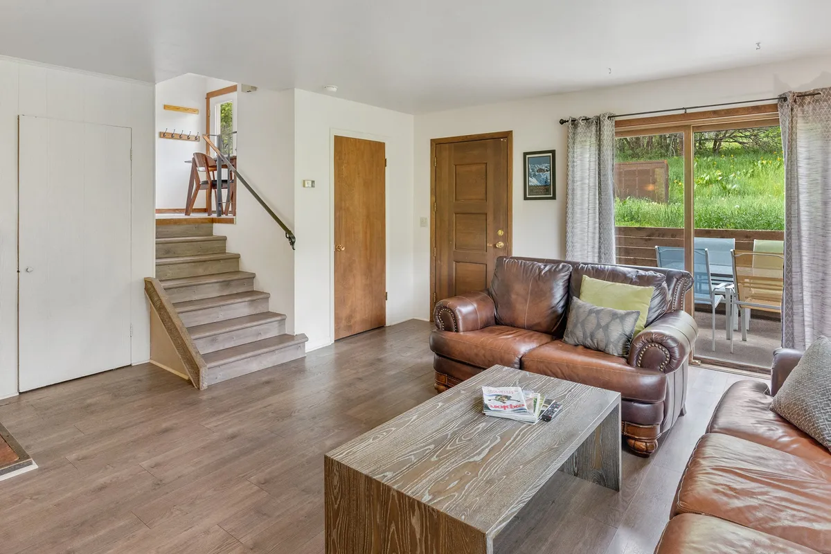 A comfortable living room scene with a leather sofa, wooden coffee table, and expansive windows. The room feels bright and airy, perfect for lounging, conversation, or entertaining guests.
