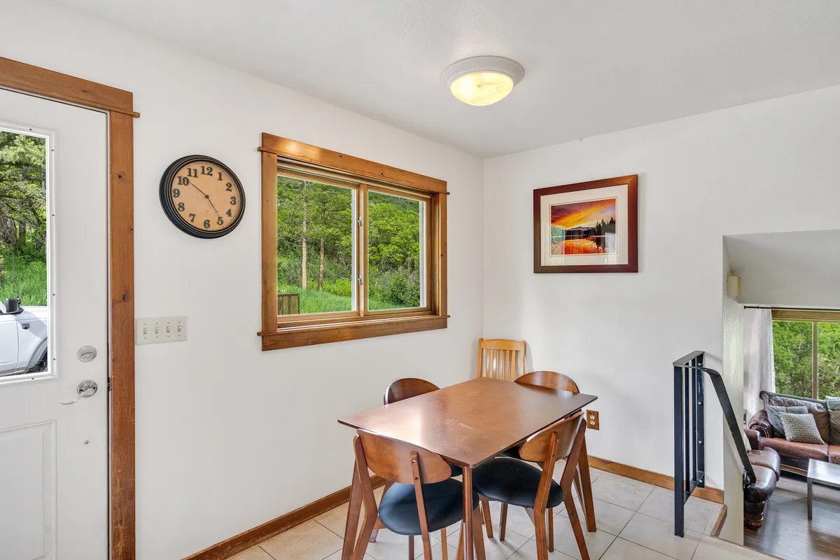 A cozy dining area with a central dining table, large window providing natural light, a wall clock, and framed artwork. The space is designed for comfort, inviting families and friends to sit together, share meals, and create lasting memories while enjoying the mountain scenery outside.