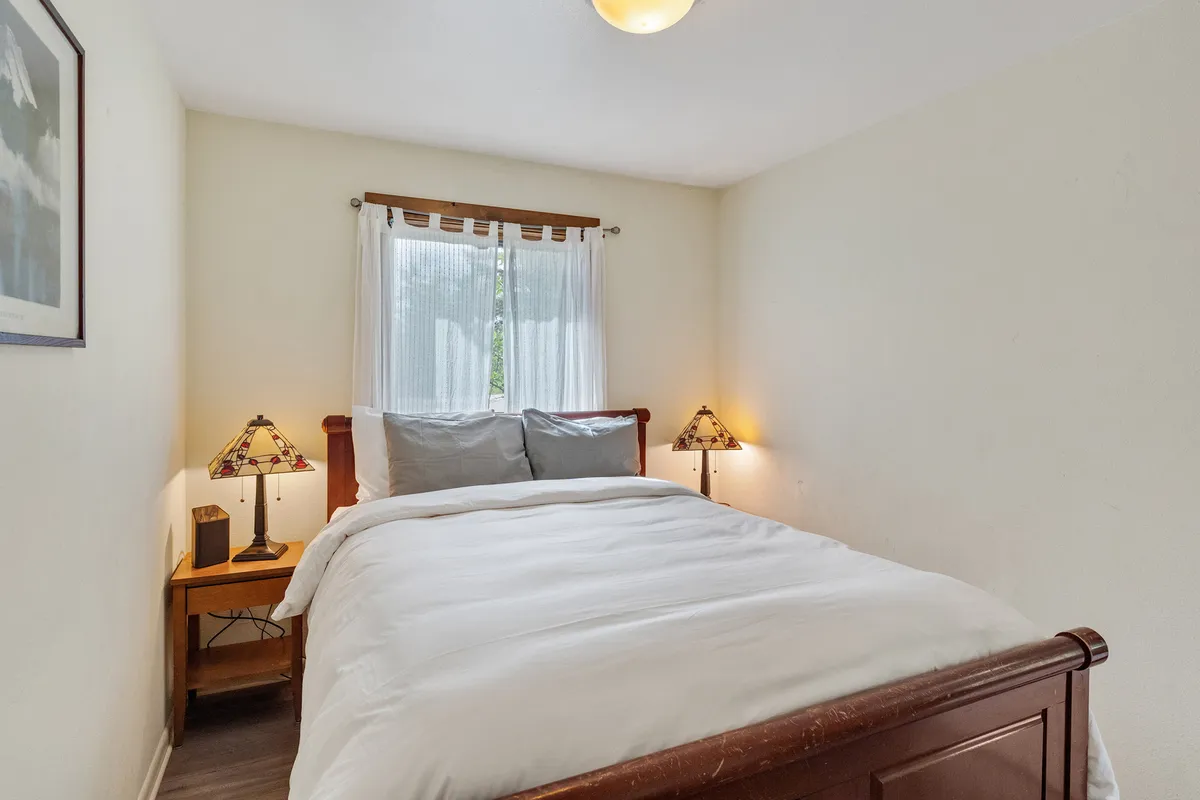 A calm, inviting bedroom dominated by a cozy bed, soft lighting from lamps, and a window that hints at the outdoors. The overall setting invites peaceful rest and relaxation.